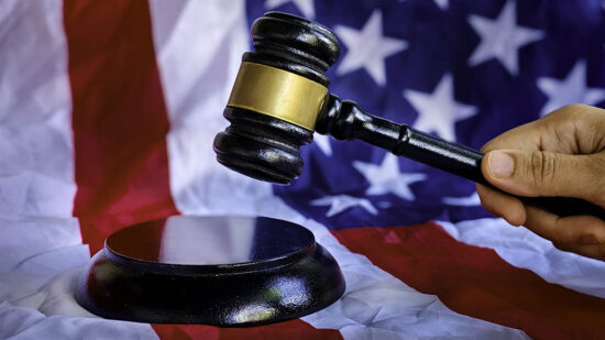 A hand holding gavel with background of usa flag.