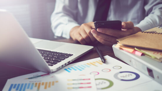 businessman hand working smart phone on wooden desk in office in morning light. The concept of modern work with advanced technology. vintage effect