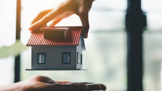 Business woman holding home miniature in office bureau. insurance protective hand over house for protection and care, Concept of home and real estate Property insurance.